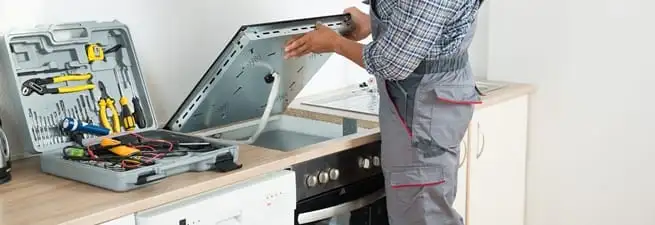 Cooktop repair technician lifting a built-in stovetop for service in Ann Arbor, MI