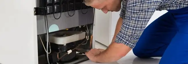 Refrigerator repair technician servicing the compressor and condenser area in Ann Arbor, MI