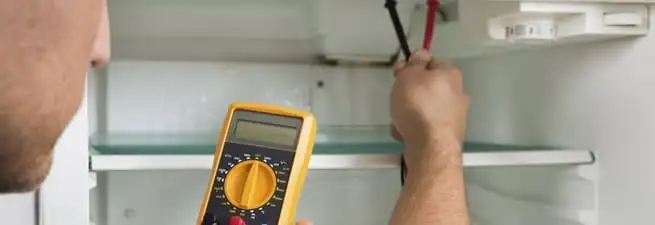 Refrigerator repair technician testing electrical components with a multimeter in Ann Arbor, MI